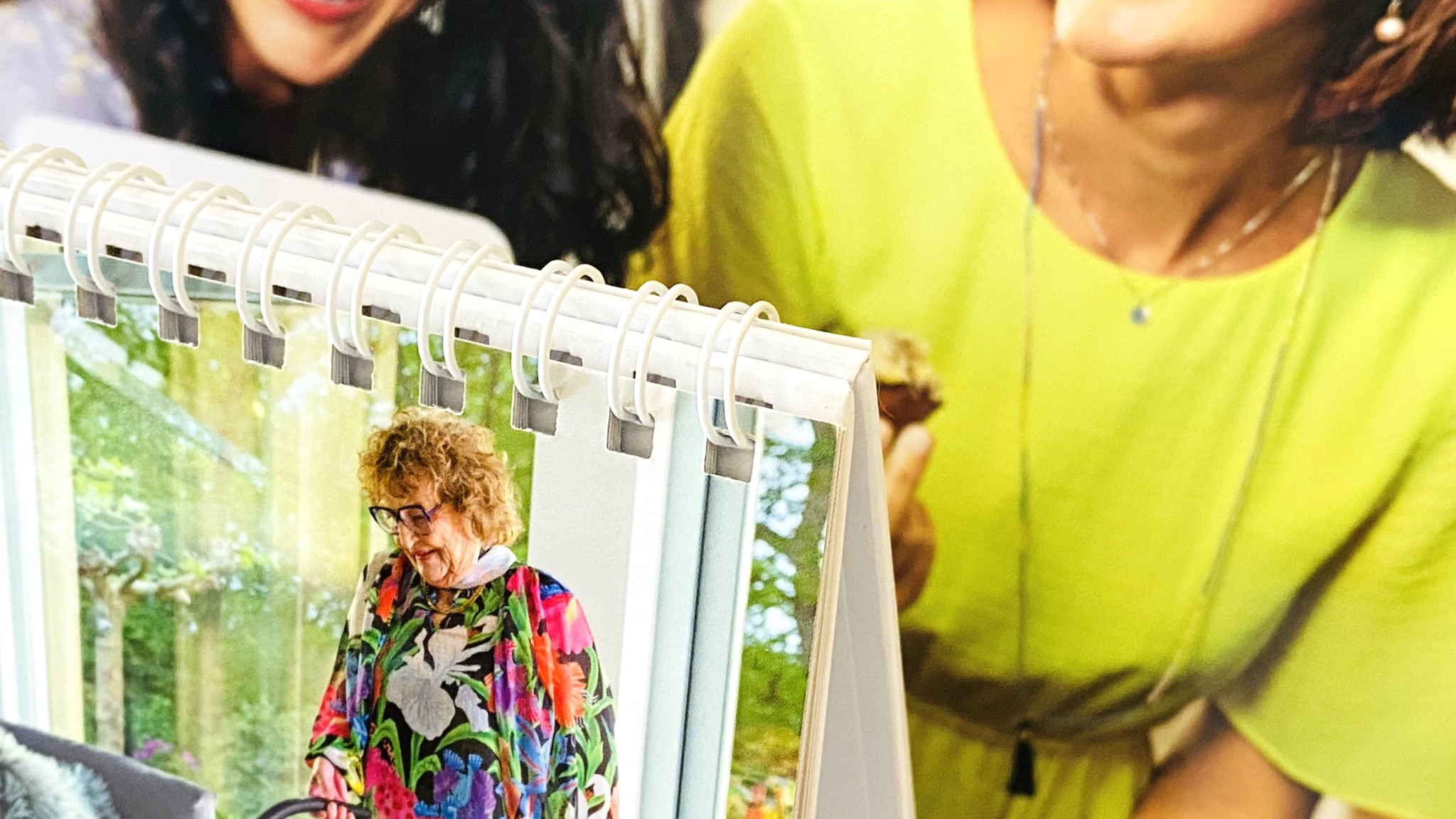 Kalendarz biurkowy ze zdjęciem starszej kobiety we wnętrzu, trzymany przez dwie osoby we Wrocławiu, widoczne spirale i kartki kalendarza.