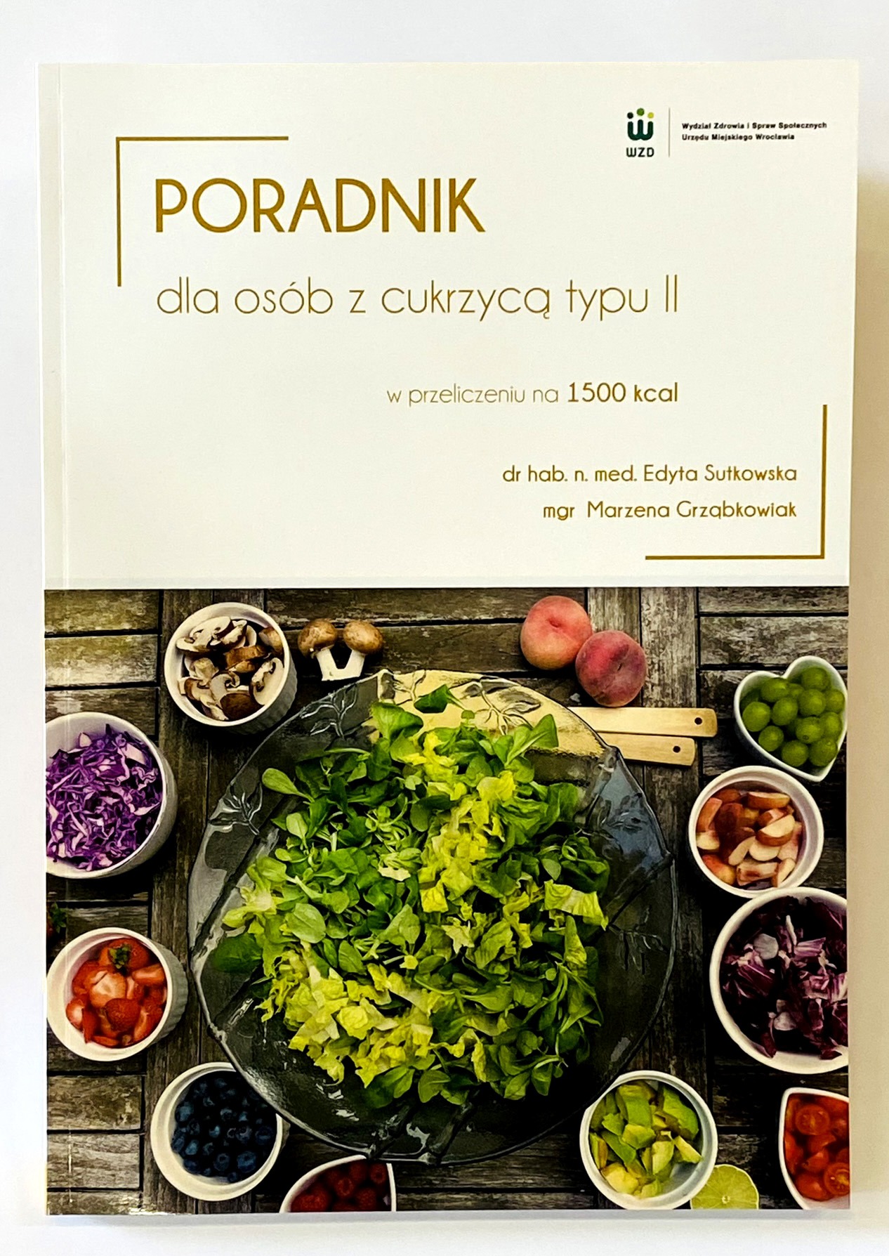 Okładka poradnika dla osób z cukrzycą typu II, prezentująca kompozycję świeżych warzyw i owoców ułożonych wokół miski z sałatą na drewnianym tle.
