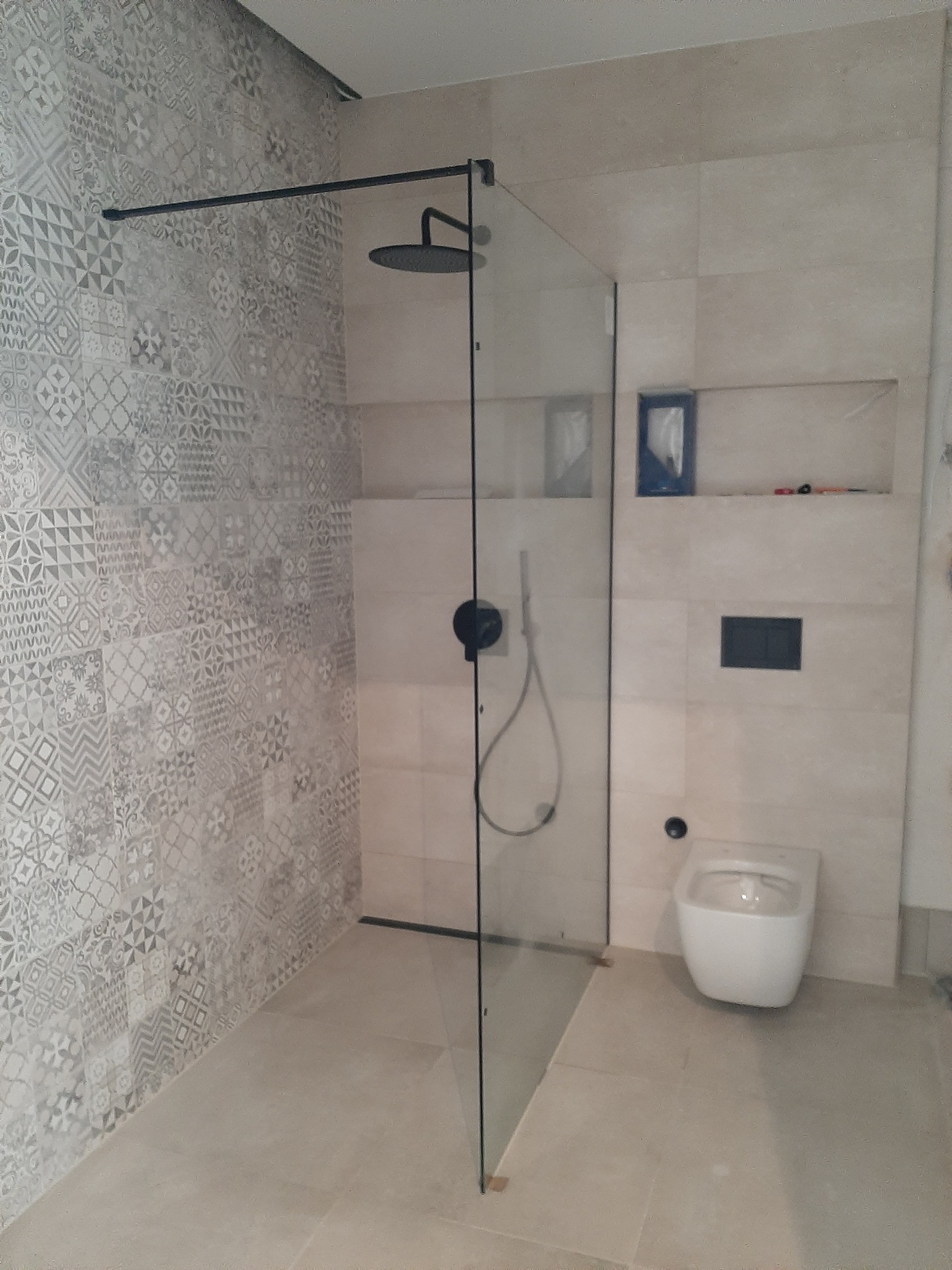 Nowoczesna łazienka z kabiną prysznicową typu walk-in z czarnymi elementami, mozaikową ścianą i podtynkową toaletą.