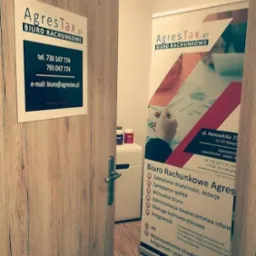Wejście do biura rachunkowego AgresTax.pl, widoczna tabliczka z numerami telefonów i adresem e-mail oraz roll-up reklamowy z ofertą usług.