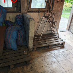 Jhhh - Wnętrze po sprzątaniu: worki z odpadami na paletach, drabina oparta o ścianę. Widoczny napis 'PO' na szybie okna, sugerujący stan po usłudze.