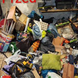 Jhhh - Zdjęcie zagraconego pomieszczenia z napisem 'Przed' w czerwonym kolorze. Widoczne kartony, puszki, worki i inne przedmioty. Na półce narzędzia i akcesoria.