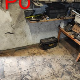 Jhhh - Półka warsztatowa z narzędziami i skrzynkami, widok na brudną podłogę z płytek. Na ścianie napis 'PO' sugerujący stan po sprzątaniu.