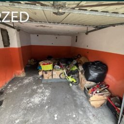 Jhhh - Zagracony garaż w Rudzie Śląskiej przed opróżnianiem. Pomieszczenie z pomarańczowymi ścianami, pełne kartonów, worków i dziecięcego rowerka. Widoczny napis 'PRZED'.