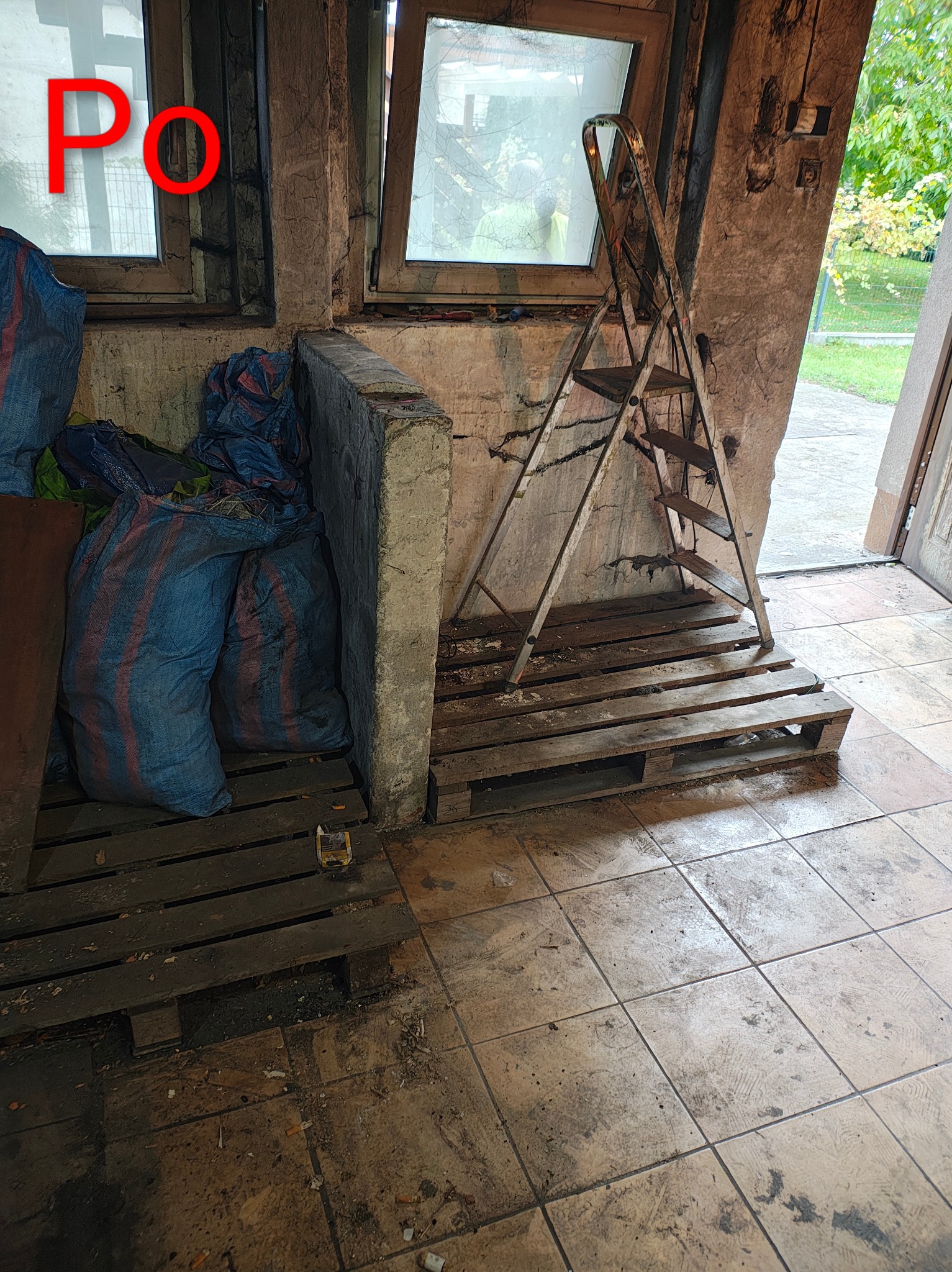 Wnętrze po sprzątaniu: worki z odpadami na paletach, drabina oparta o ścianę. Widoczny napis 'PO' na szybie okna, sugerujący stan po usłudze.