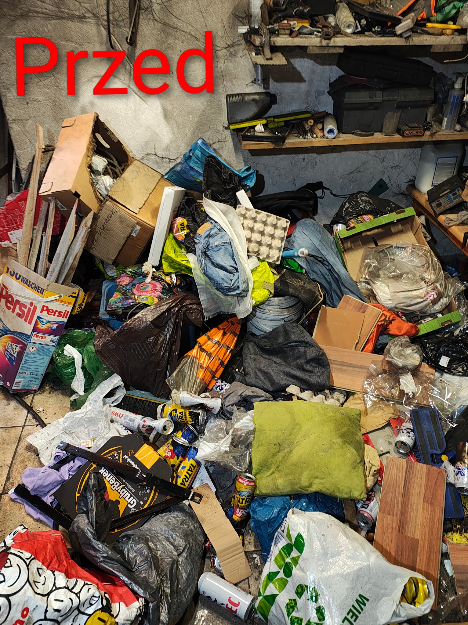 Zdjęcie zagraconego pomieszczenia z napisem 'Przed' w czerwonym kolorze. Widoczne kartony, puszki, worki i inne przedmioty. Na półce narzędzia i akcesoria.