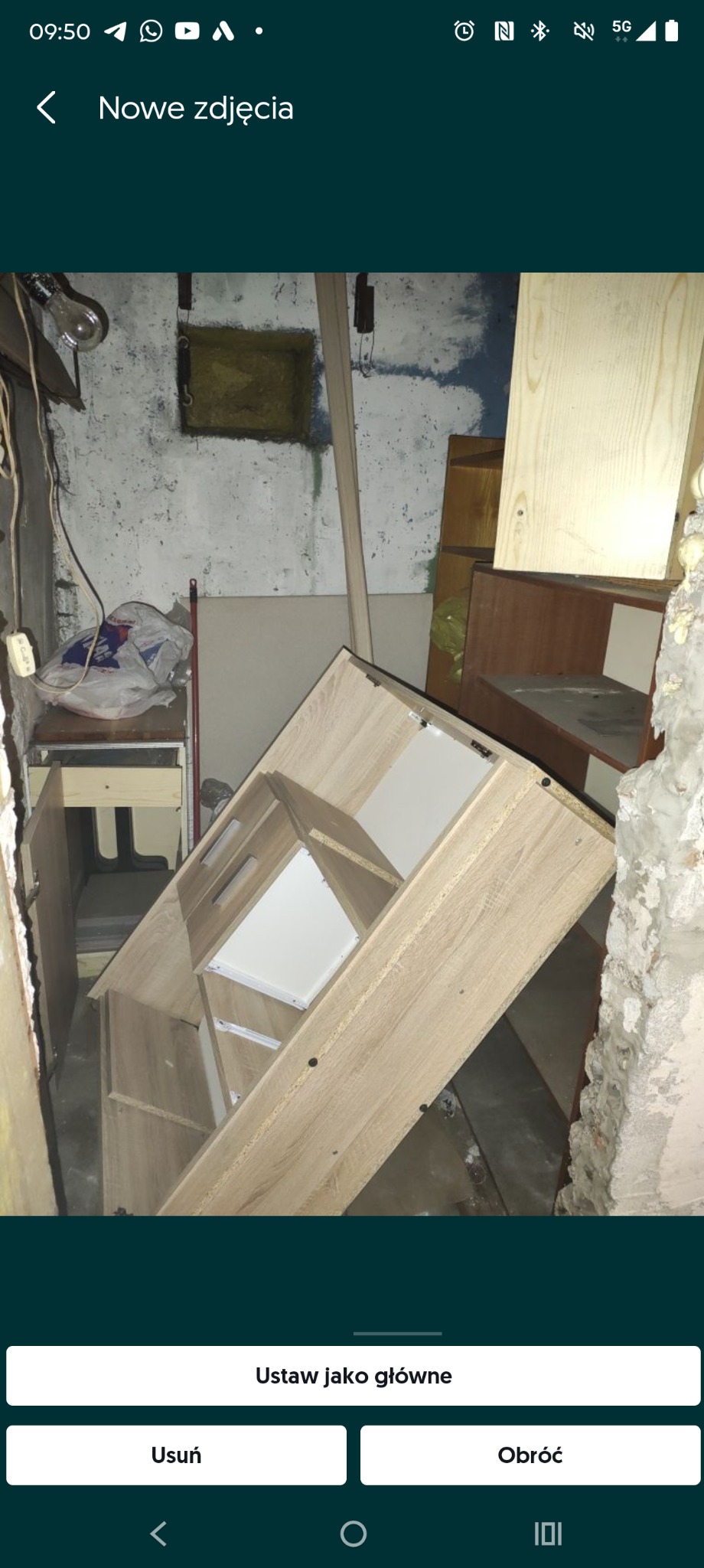 Opróżnianie piwnicy: przewrócony regał z jasnego drewna na tle surowych ścian i podłogi, widoczne ślady demontażu i pozostałości po remoncie. Nieuporządkowana przestrzeń.