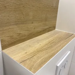 Zabudowa stelaża WC z drewnopodobną p&oacute;łką i białymi płytkami, widoczny przycisk spłukujący.