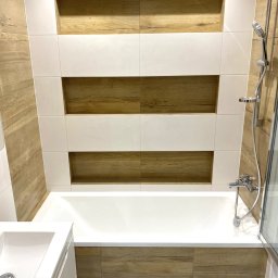 Domowa Przestrzeń Dawid Rogacki - Nowoczesna łazienka z wanną obudowaną płytkami imitującymi drewno, białe płytki z wnękami na ścianie i marmurowa podłoga.