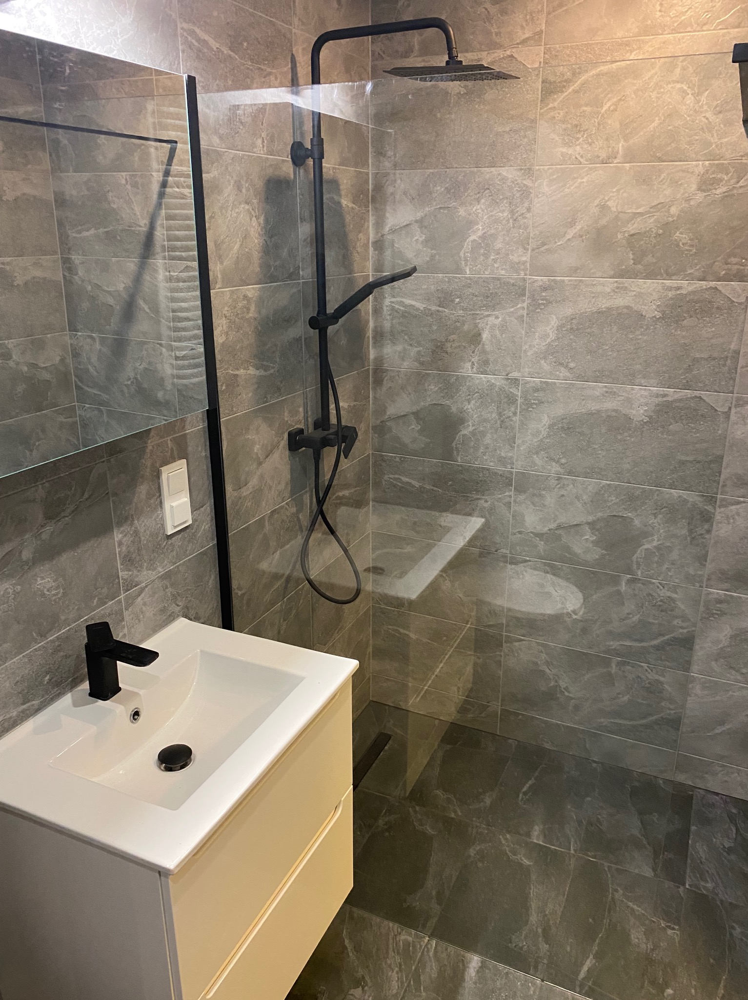 Nowoczesna łazienka z szarymi płytkami imitującymi marmur, czarną armaturą i białą szafką pod umywalką.