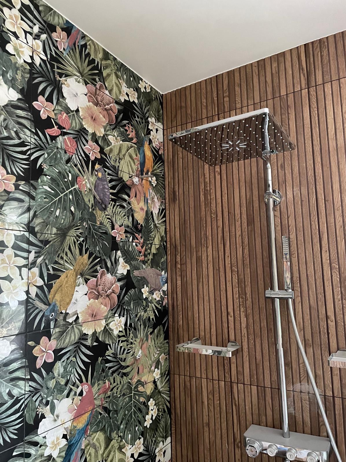 Kabina prysznicowa z deszczownicą, ściana z płytek z motywem tropikalnych roślin i papug, druga ściana z paneli imitujących drewno.