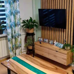 Stół z drewna z żywicą epoksydową w kolorze turkusowym, czarne metalowe nogi, na tle drewnianej ściany z lameli i szafki RTV, dywan w geometryczny wzór.