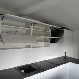 Meble Skrobisz - Biała kuchnia z czarnym blatem, szafki górne otwierane do góry z widocznymi mechanizmami, czarny okap i zlew, oświetlenie LED pod szafkami.