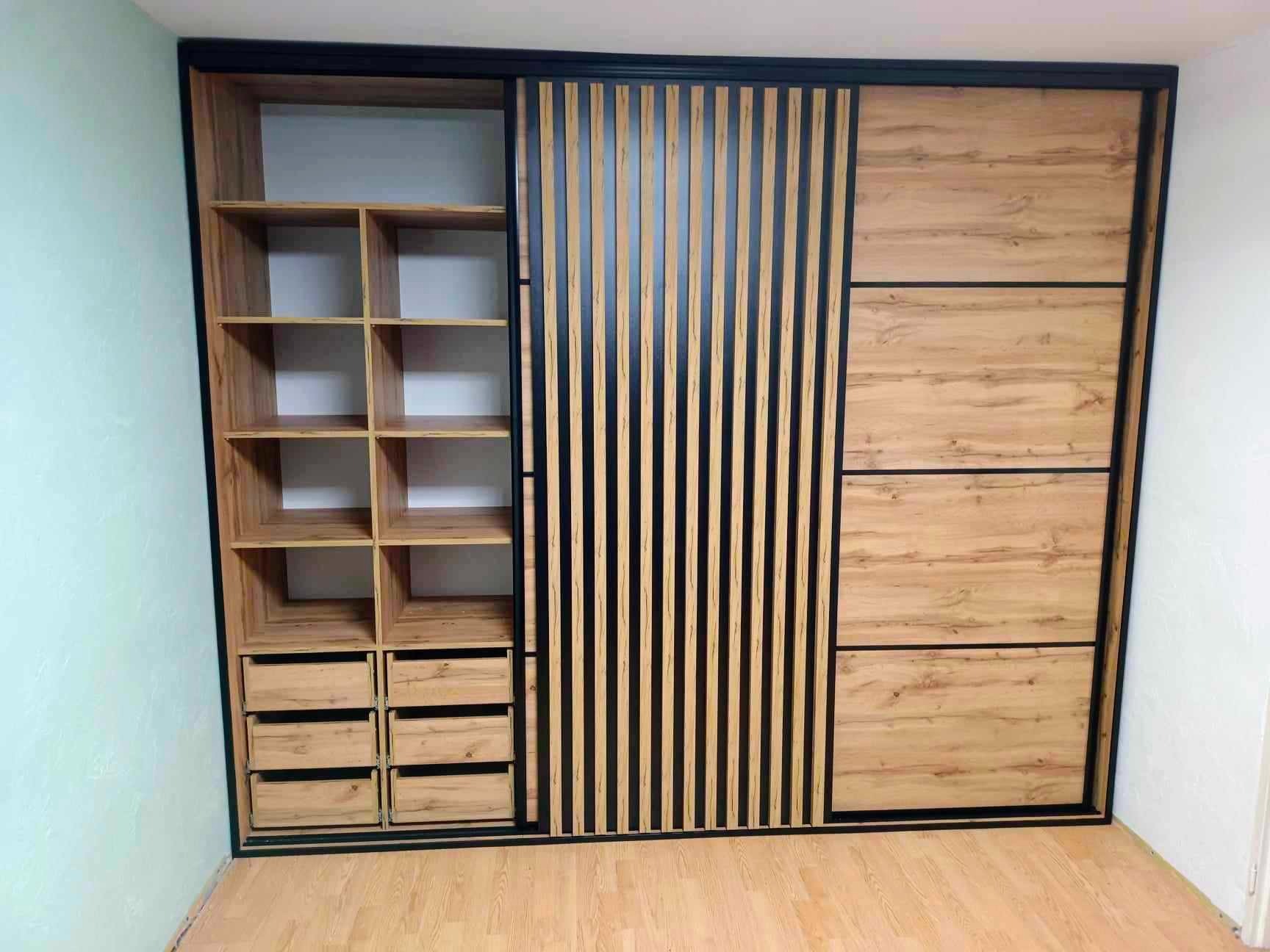 Nowoczesna szafa wnękowa z przesuwnymi drzwiami: część z półkami i szufladami, część z lamelami w czarnej ramie, wykończenie w odcieniach drewna.