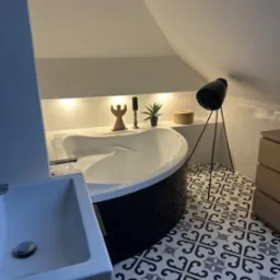 Nowoczesna łazienka na poddaszu z wolnostojącą wanną obudowaną czarną mozaiką, wzorzystą podłogą, oświetleniem LED w niszy i czarną lampą na trójnogu.