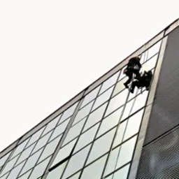 Dwóch alpinistów na linach czyści szklaną fasadę biurowca z otwartym oknem, widok z dołu.