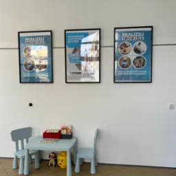 Poczekalnia z dziecięcym stolikiem i krzesłami, na ścianie wiszą oprawione plakaty z hasłem 'Realizuj swoje cele' i logo firmy finansowej oferującej kredyty i pożyczki.