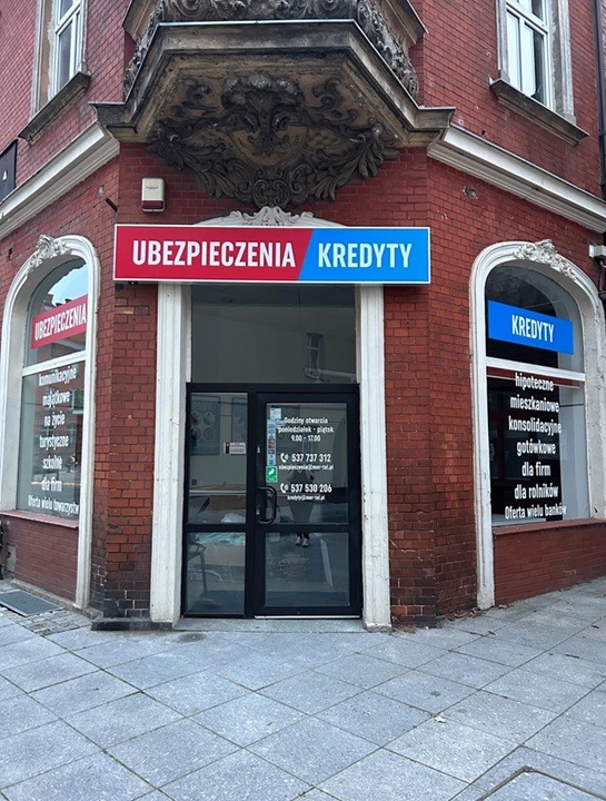 Fasada budynku z szyldem 'Ubezpieczenia Kredyty', okna z informacjami o ofercie, wejście z godzinami otwarcia i numerami telefonów.