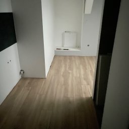 Stanislav Papkov - Nowo ułożona, jasna podłoga z paneli w odcieniach beżu, widoczna przy białych ścianach i elementach instalacji elektrycznej. W tle biała szafka rewizyjna na ścianie.