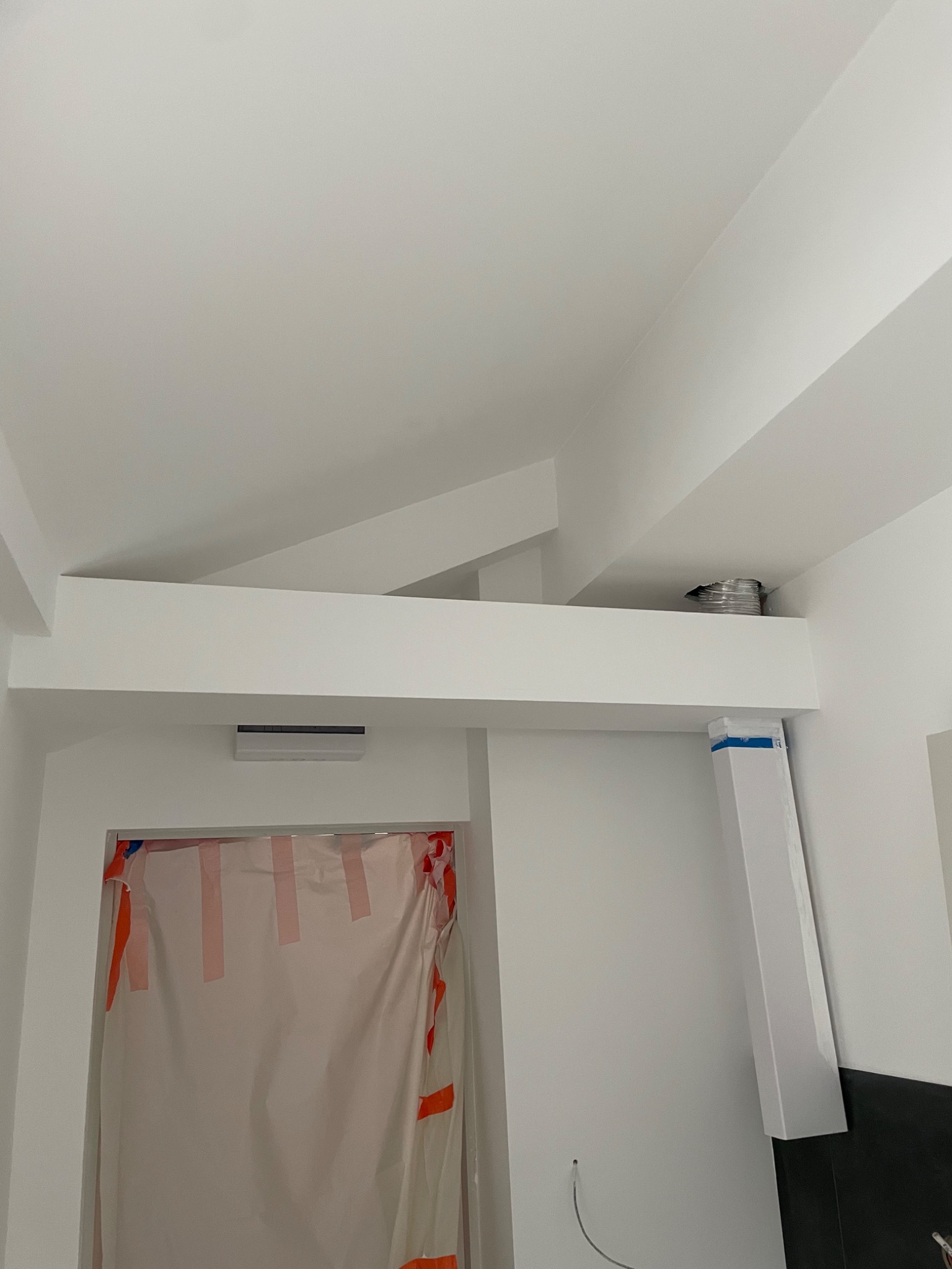 Wnętrze w trakcie prac wykończeniowych: zabezpieczone folią drzwi, pomalowany sufit z widocznymi belkami, zamontowany klimatyzator i fragment wentylacji.