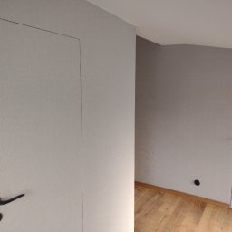 R-F Remonty - Dwie ukryte drzwi w szarej ścianie z tapetą o delikatnej fakturze, czarne klamki, drewniana podłoga