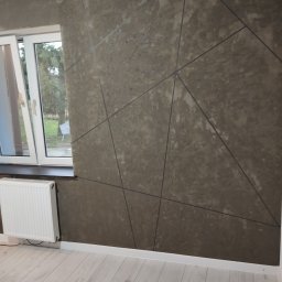 R-F Remonty - Ściana wykończona gładzią strukturalną w odcieniach szarości z geometrycznym wzorem, biała listwa przypodłogowa i grzejnik, panele podłogowe imitujące drewno.