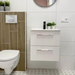 Nowoczesna łazienka po remoncie: białe płytki, wisząca szafka z umywalką, czarna bateria, okrągłe lustro i wzorzysta podłoga.