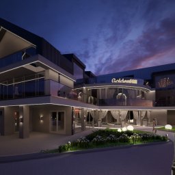 Witwicki Architekt - projekty elewacji - Nowoczesny budynek 'GoldenHill' oświetlony nocą, widziany przez kobietę w VR, prezentujący projekt elewacji z elementami szklanymi i minimalistycznym oświetleniem.