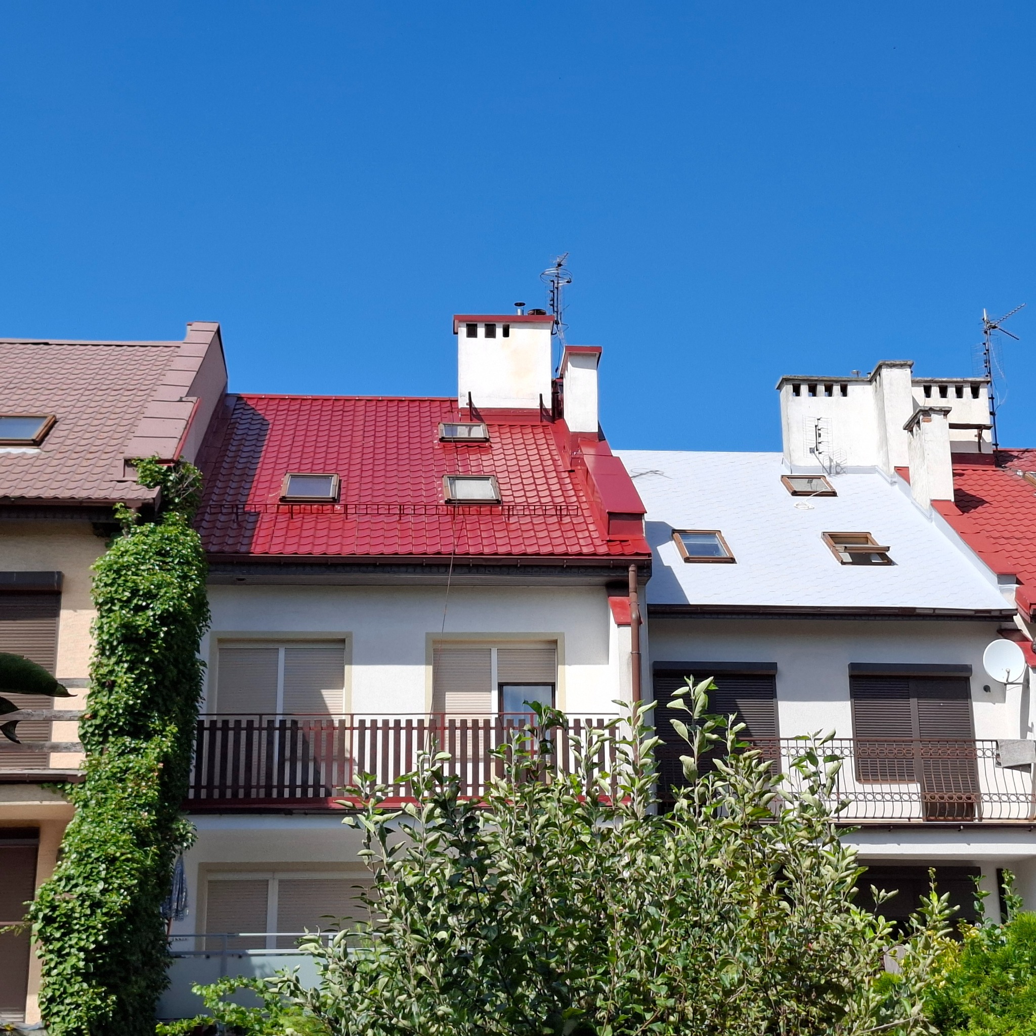 Dwa dachy po renowacji: czerwony RAL 3009 i jasnoszara membrana hydroizolacyjna PWP100 na gont bitumiczny. Widoczne okna dachowe i balkony.