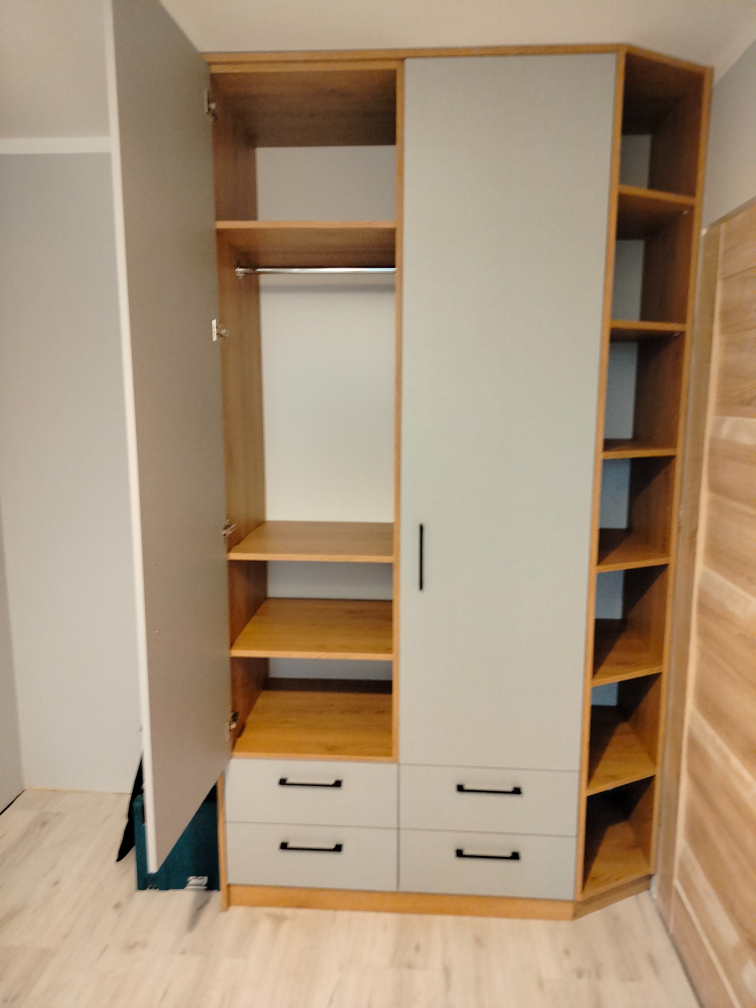 Szara szafa z drewnianymi półkami i szufladami, jedna strona otwarta, z widocznymi półkami i drążkiem na ubrania.