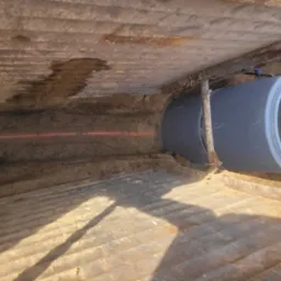 Betonowa rura kanalizacyjna w wykopie, widoczny laser wyznaczający poziom oraz szalunek zabezpieczający ściany wykopu.