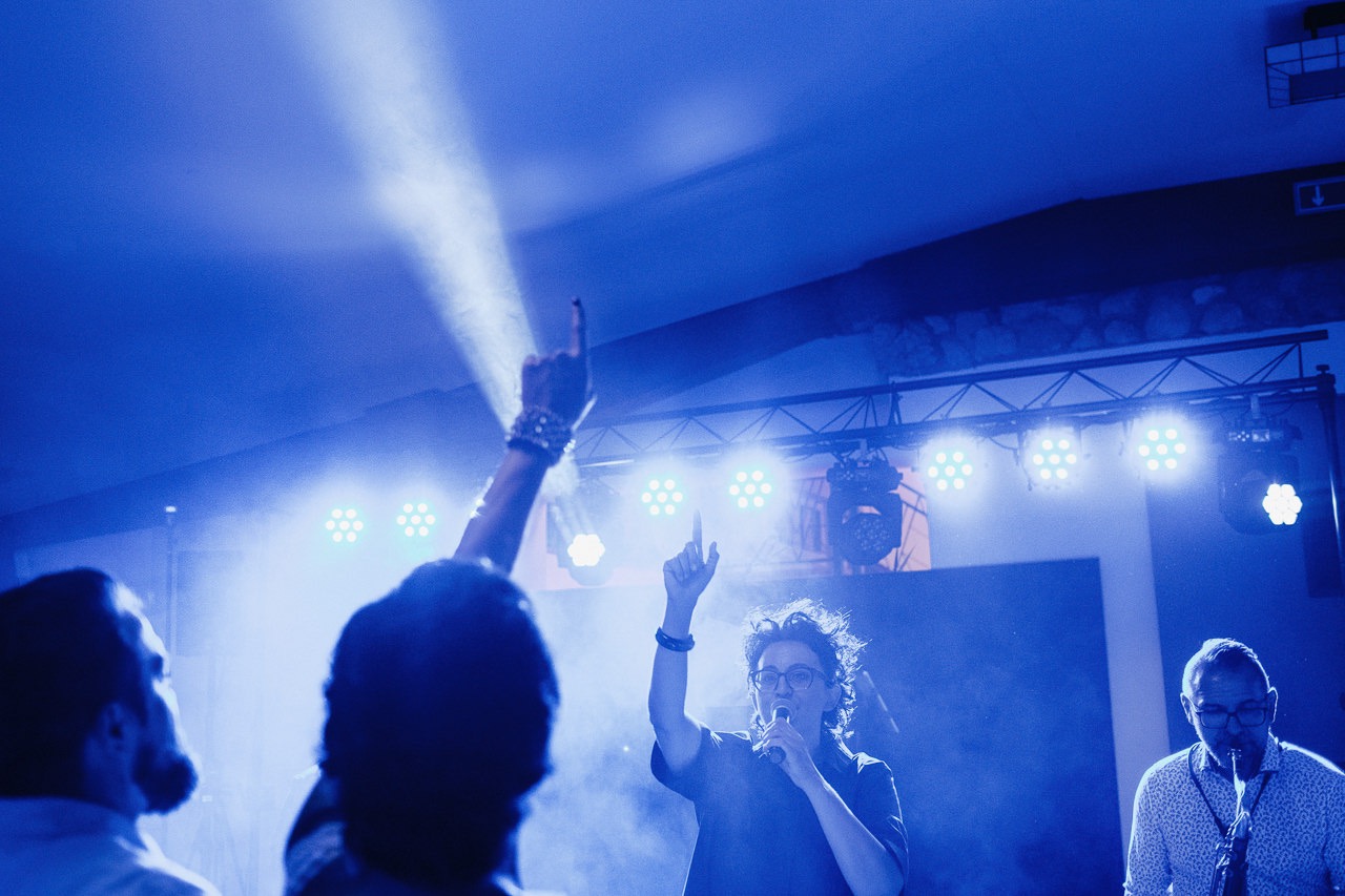 Koncert w Katowicach: wokalistka z mikrofonem na scenie w niebieskim oświetleniu, publiczność z podniesionymi rękami, saksofonista w tle.