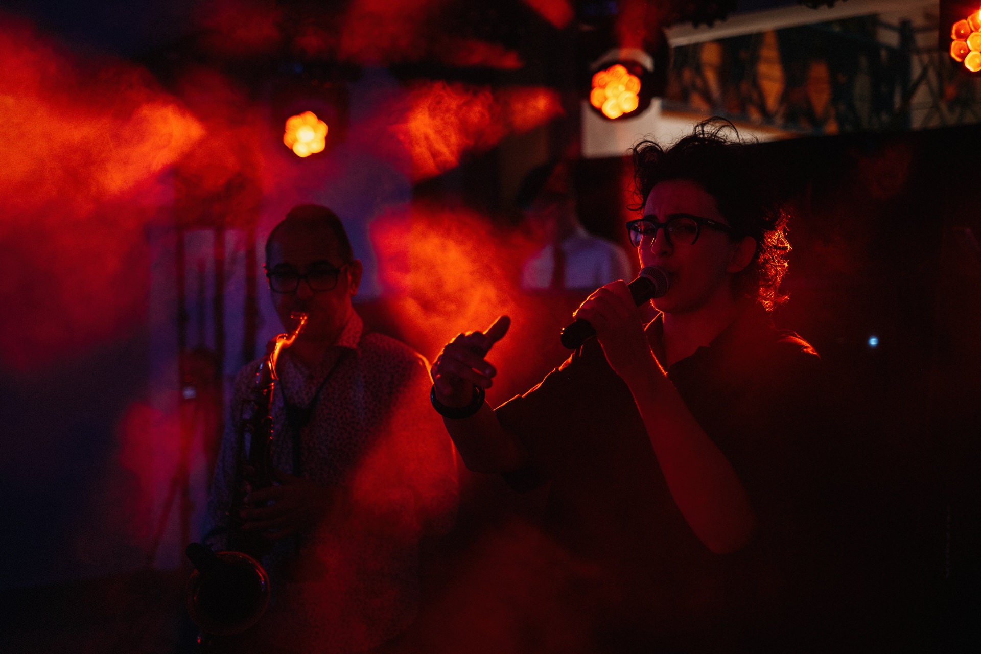 Wokalista z mikrofonem i saksofonista w czerwonym oświetleniu scenicznym podczas występu na evencie.