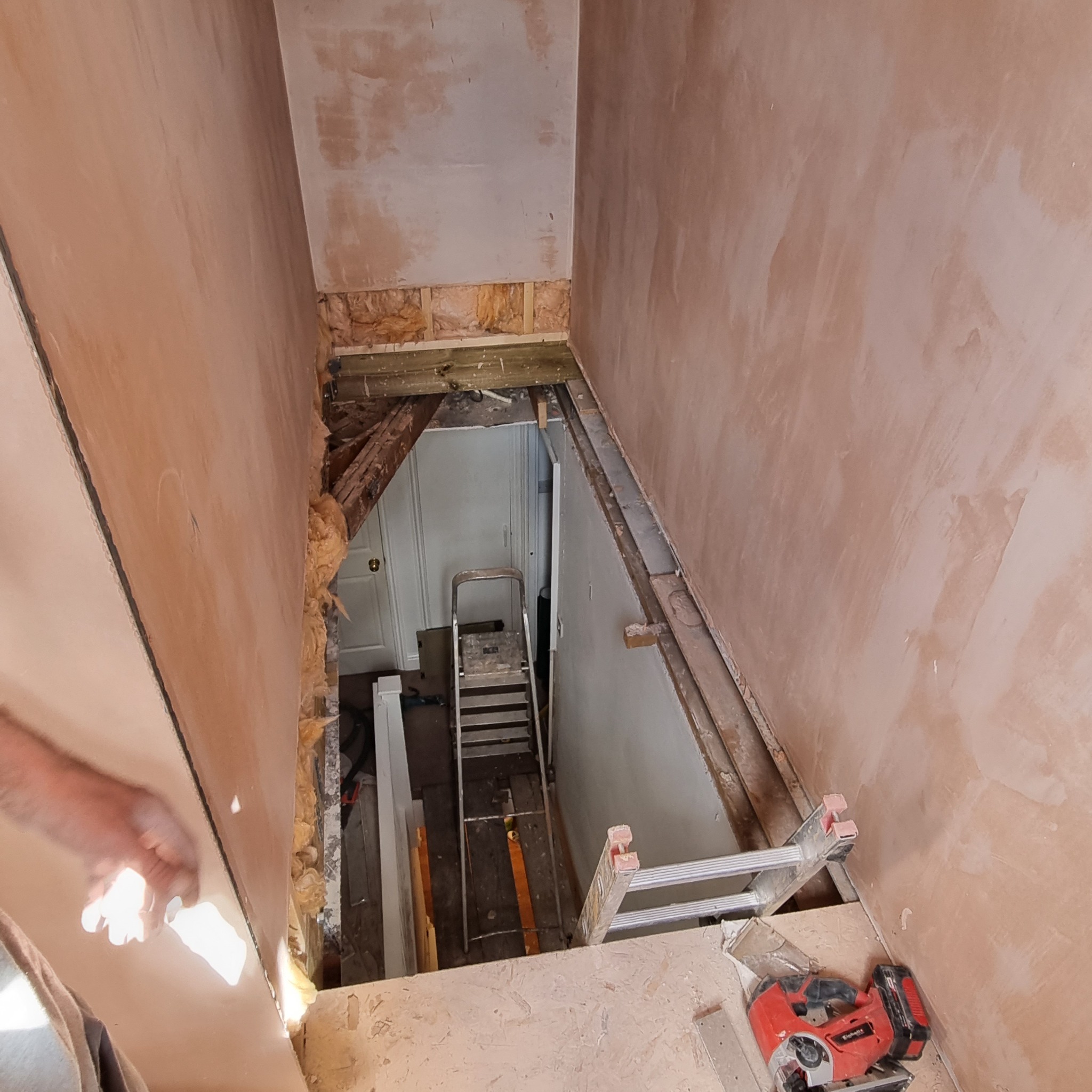 Wnętrze w trakcie remontu: ściany pokryte świeżym tynkiem, widoczne elementy konstrukcyjne, drabina w głębi pomieszczenia i czerwona wyrzynarka Einhell na podłodze.