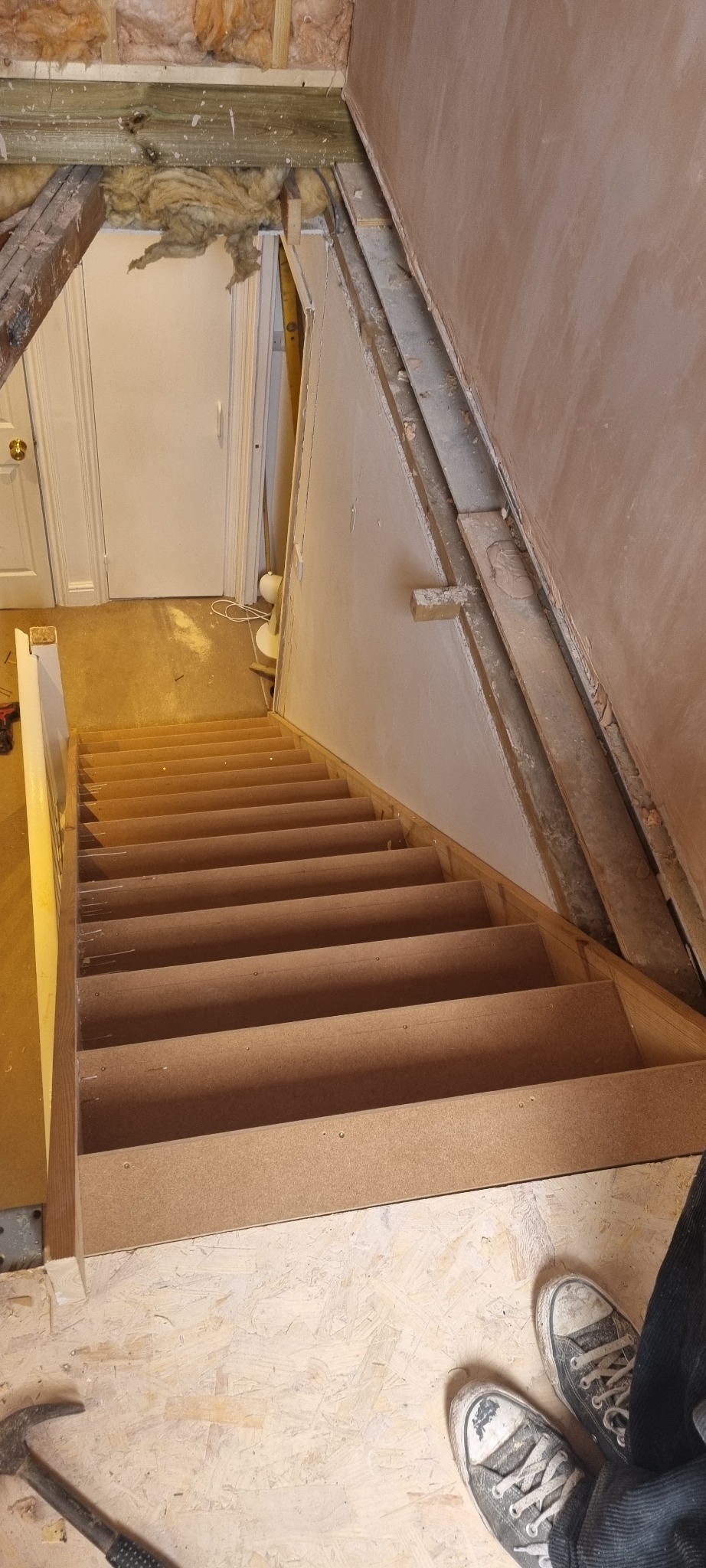 Montaż nowych schodów z surowego drewna w trakcie remontu, widoczne niedokończone ściany, izolacja i narzędzia.