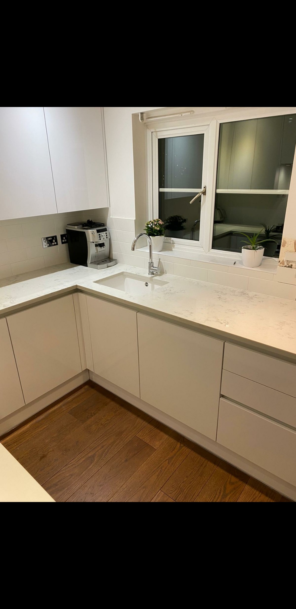 Nowoczesna, jasna łazienka z białymi szafkami, blatem z delikatnym wzorem, chromowaną armaturą, ekspres do kawy na blacie i drewnianą podłogą.