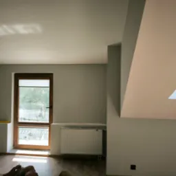 Świeżo pomalowane wnętrze poddasza we Włocławku z oknem dachowym, grzejnikiem i widocznym poziomem na ścianie, w tle odpoczywający mężczyzna.