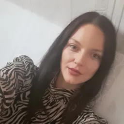 Portret kobiety z ciemnymi włosami w bluzce w zebrę na tle jasnej ściany z delikatnym wzorem.