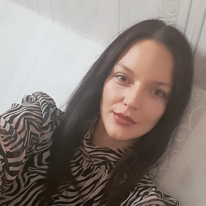 Portret kobiety z ciemnymi włosami w bluzce w zebrę na tle jasnej ściany z delikatnym wzorem.