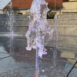 Wodotrysk z podświetleniem LED w miejskiej przestrzeni, w tle budynek z czerwoną dachówką.