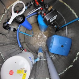 M.R.Service Michał Rowicki - Wnętrze betonowej studni z zainstalowanym systemem uzdatniania wody: zbiorniki, filtry i rury w odcieniach błękitu, szarości i czerni, widok z góry.