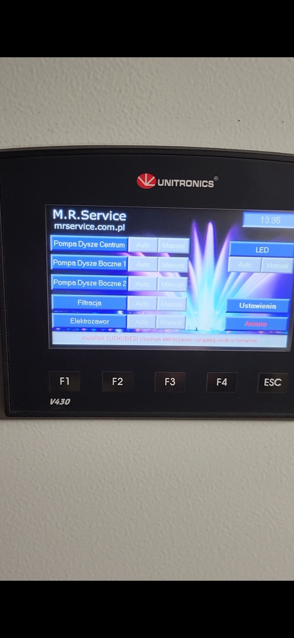 Panel sterowania Unitronics V430 z interfejsem do zarządzania pompami dysz fontanny, filtracją i elektrozaworem, wyświetlający komunikat o awarii suchobiegu.