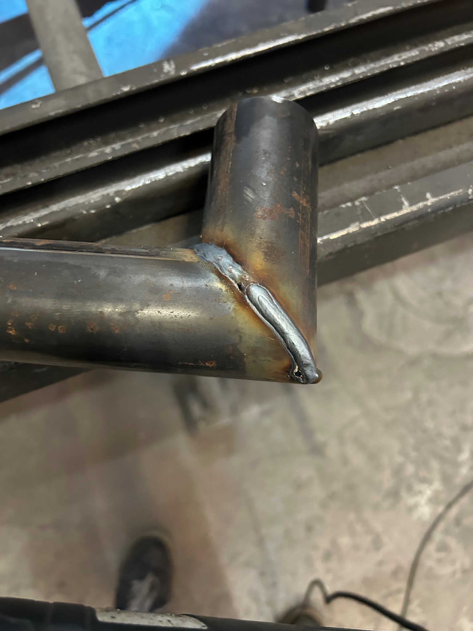 Spoina łącząca rury pod kątem prostym, wykonana w Jastrzębiu-Zdroju. Widoczne ślady rdzy na metalu, co sugeruje pracę w warsztacie lub na zewnątrz.