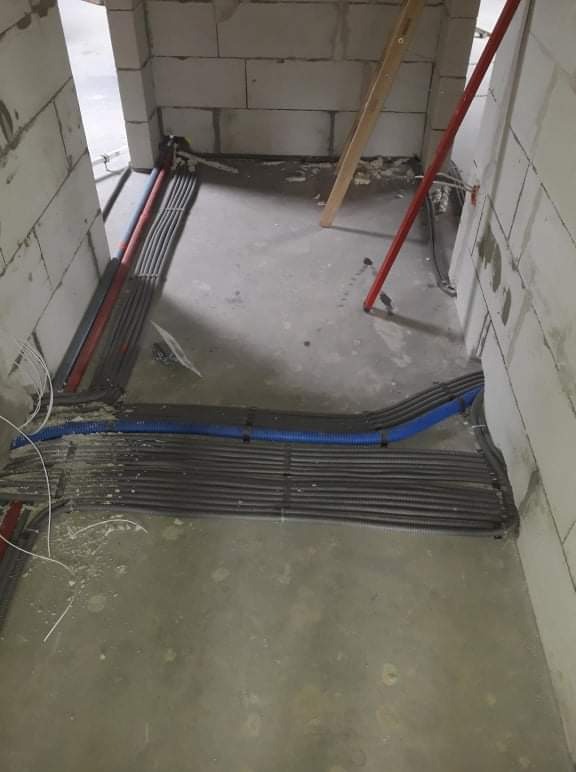 Wiązki przewodów elektrycznych w peszlach ułożone na surowym betonie, w trakcie prac instalacyjnych w pomieszczeniu z bloczków betonowych.