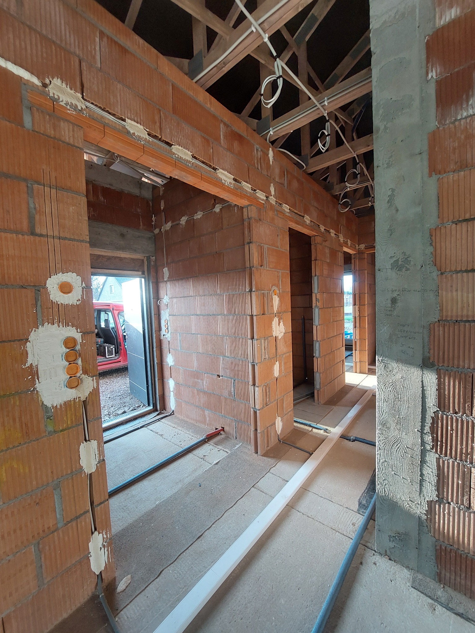 Wnętrze domu w trakcie budowy z widocznymi przewodami elektrycznymi poprowadzonymi pod sufitem i w ścianach z pustaków ceramicznych, osadzone puszki elektryczne z pomarańczowymi wkładami, surowy...