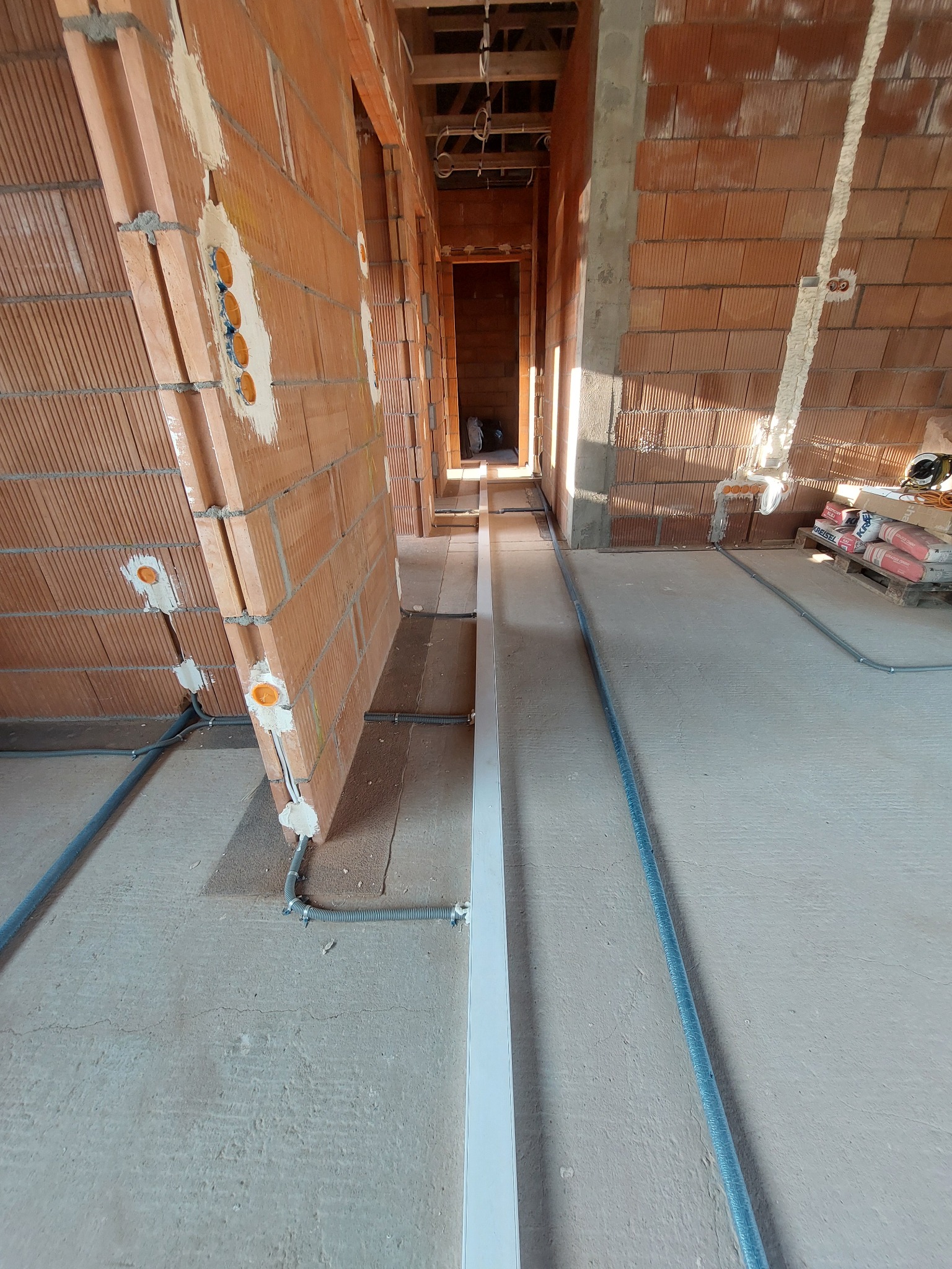 Wnętrze w trakcie budowy z widocznymi przewodami elektrycznymi w peszlach ułożonymi na podłodze i puszkami elektrycznymi w ścianach z czerwonej cegły.