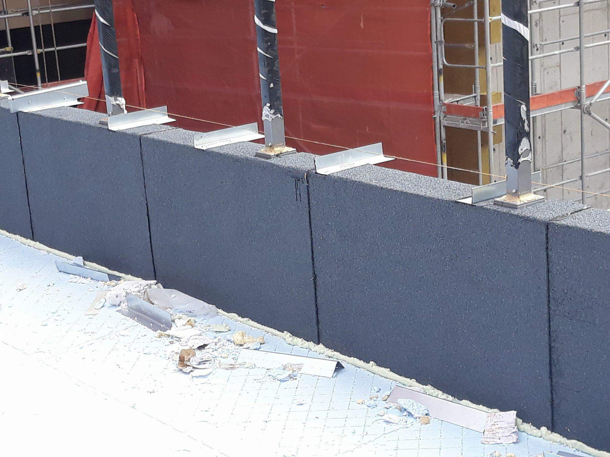 Montaż izolacji termicznej na dachu z widocznymi elementami mocującymi i fragmentami materiałów izolacyjnych, na tle konstrukcji rusztowania.