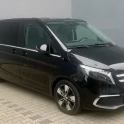 Czarny, luksusowy van Mercedes-Benz V-klasa z przyciemnianymi szybami, zaparkowany na kostce brukowej, widok z przodu i boku.