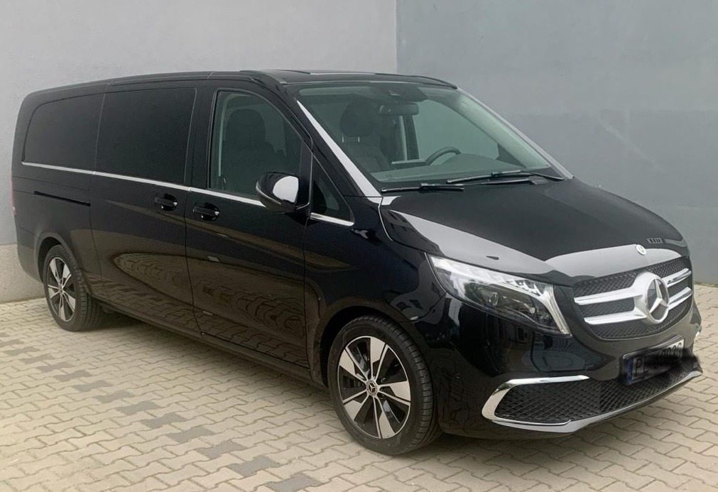Czarny, luksusowy van Mercedes-Benz V-klasa z przyciemnianymi szybami, zaparkowany na kostce brukowej, widok z przodu i boku.
