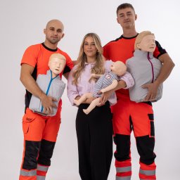 Med4Life Andrzej Olejarz - Trzy osoby pozują z manekinami do ćwiczeń resuscytacji: dwóch mężczyzn w pomarańczowo-czarnych strojach ratowniczych trzyma manekiny dorosłych, a kobieta w różowej koszuli trzyma manekin...